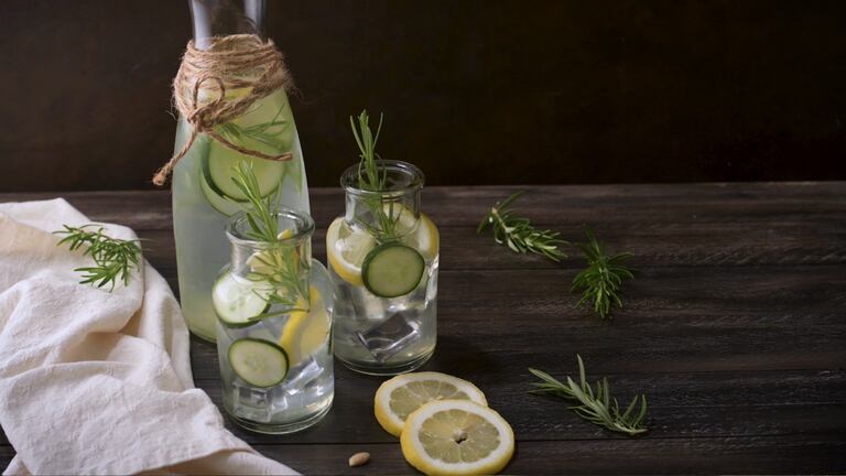 Una jarra con agua con rodajas de limón y ramitas de romero.