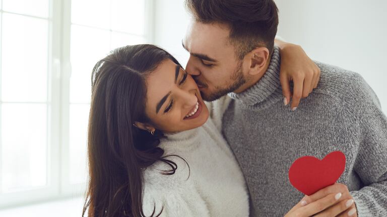 Una pareja dándose un beso mientras sostienen un corazón de papel.