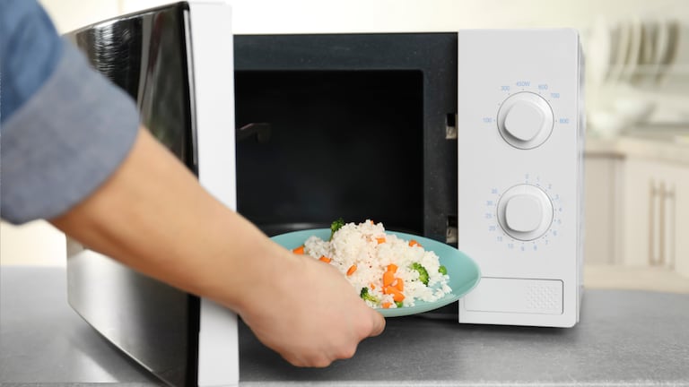 Una persona calentando comida en un microondas.