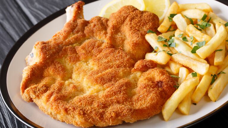 Una milanesa en un plato acompañada con papas a la francesa.