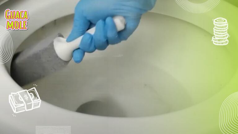 Una mano con un guante y una piedra pómez tallando la taza de baño para eliminar el sarro.