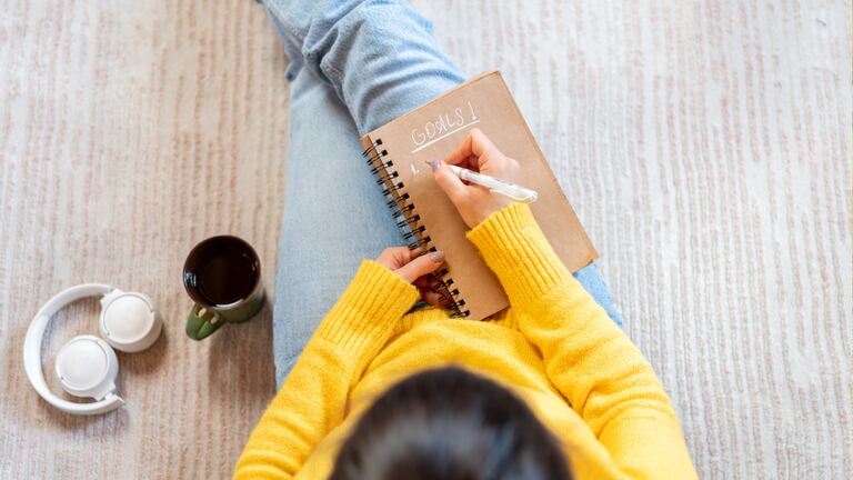 Una mujer sentada disfrutando de un café mientras escribe en una libreta.