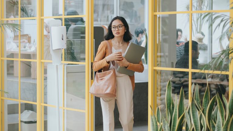 Una mujer con una laptop y un vaso de café saliendo de su trabajo.